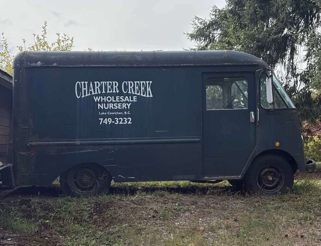 The original Charter Creek Wholesale Nursery delivery van, dark green with hand-painted lettering, parked in the grass at the farm.